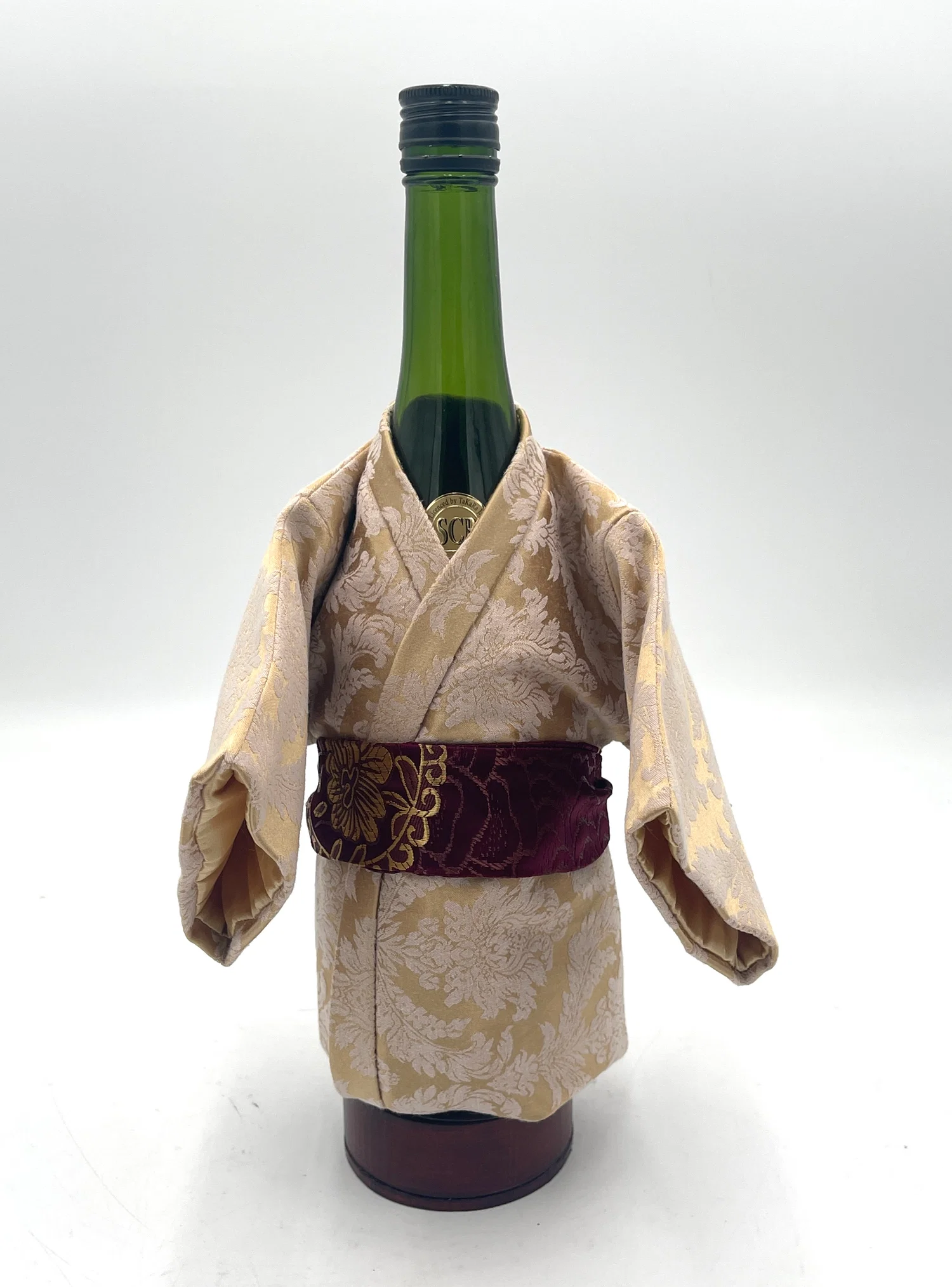 A small kimono created and fitted to house a sake bottle. It also includes a wood base on the bottom acting as a coaster.