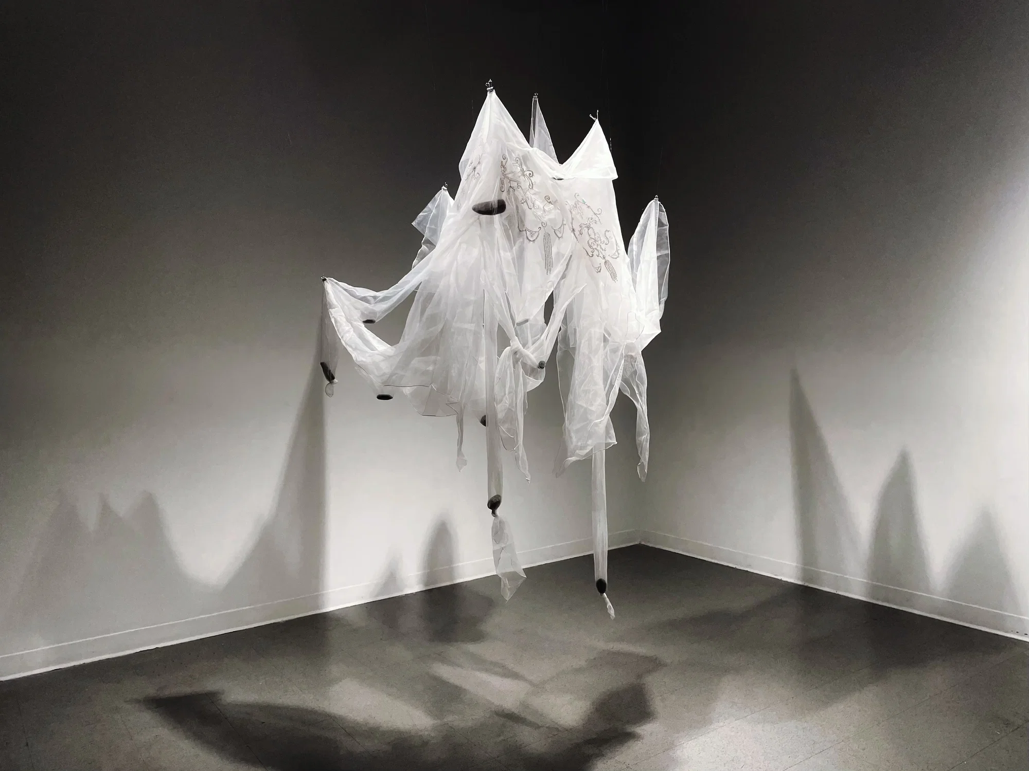 A white, translucent gauze garment hanging in mid-air, containing many scattered rocks inside.