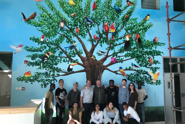 Otis group in front of a mural by Jacaranda students depicting a tree full of colorful birds