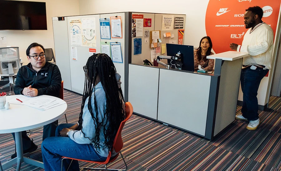 Assistant Director of Student Employment and Operations, Edward Kang, advises a student while Associate Director of Employer Engagement and Alumni Relations, Keenan Jones (far right), confers with an administrative assistant in the Career Services office.