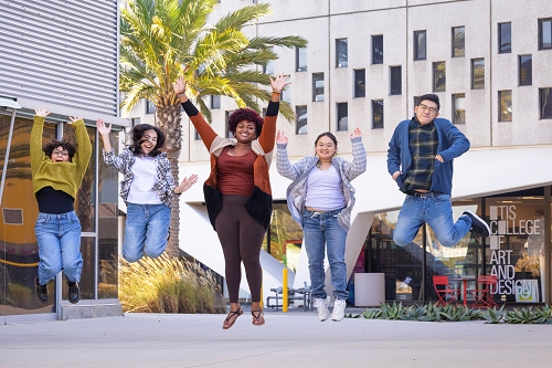 Five students outdoors on campus jumping into the air