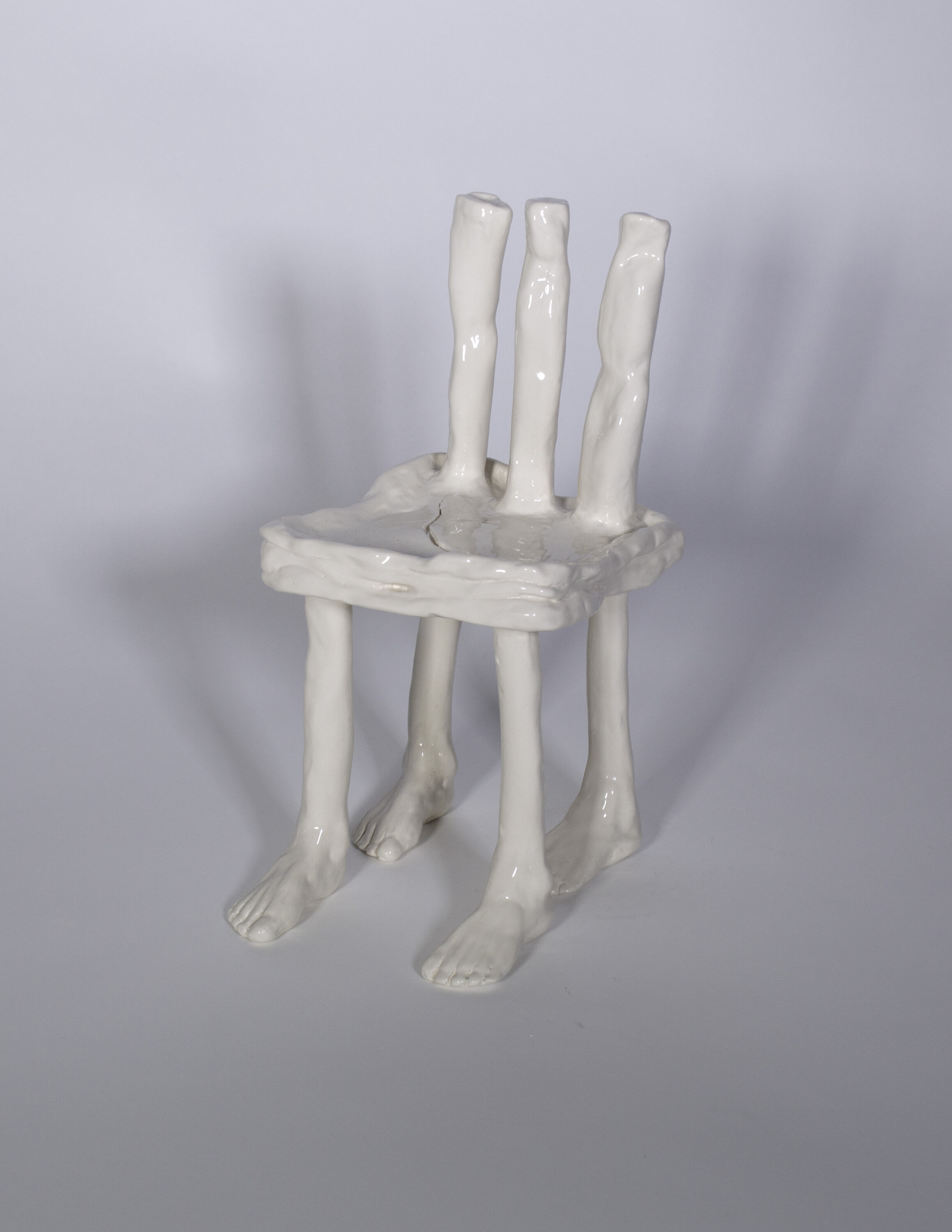 Ceramic chair. Ivory in color and has feet at the bottom of chair legs. There is a crack in the seat of the chair. Three wonky cylinders make up the back of the chair