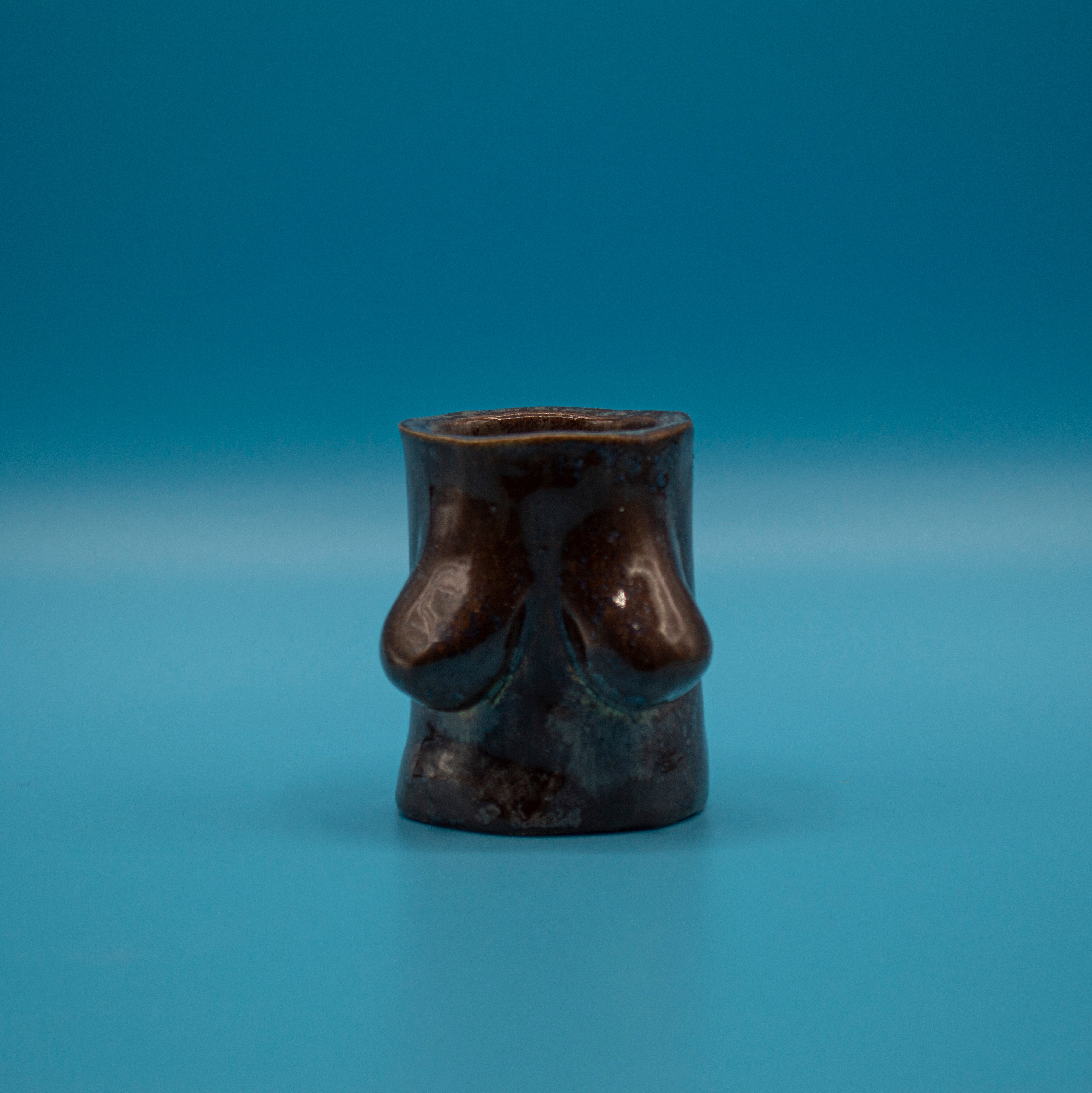Brown ceramic shot glass with slightly saggy breasts.