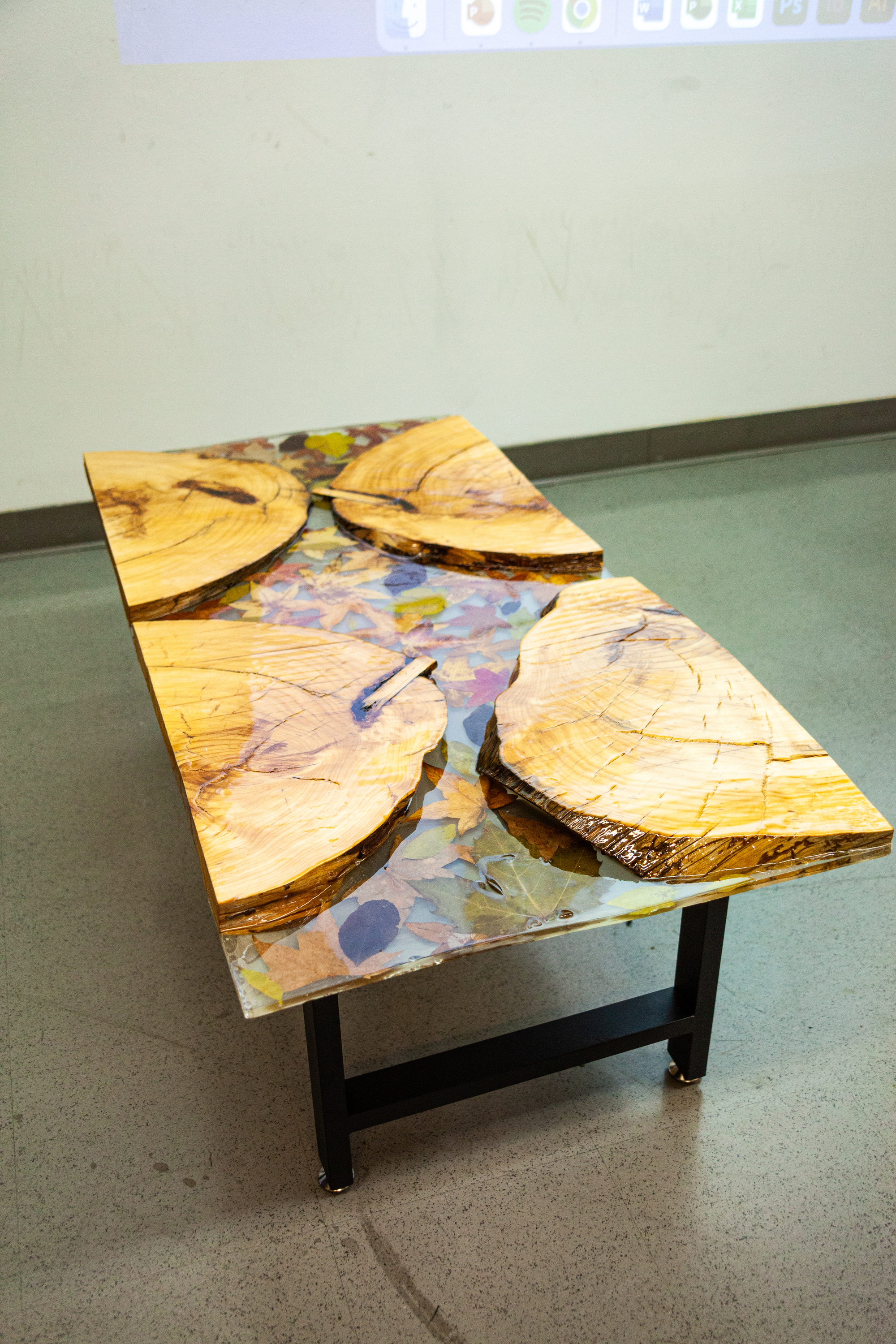 A reverse river resin coffee table made of mostly resin flows around four slices of wood that was once a tree stump. Autumn leaves have been embedded in the resin, as if the table itself were a slice of a river frozen in time.