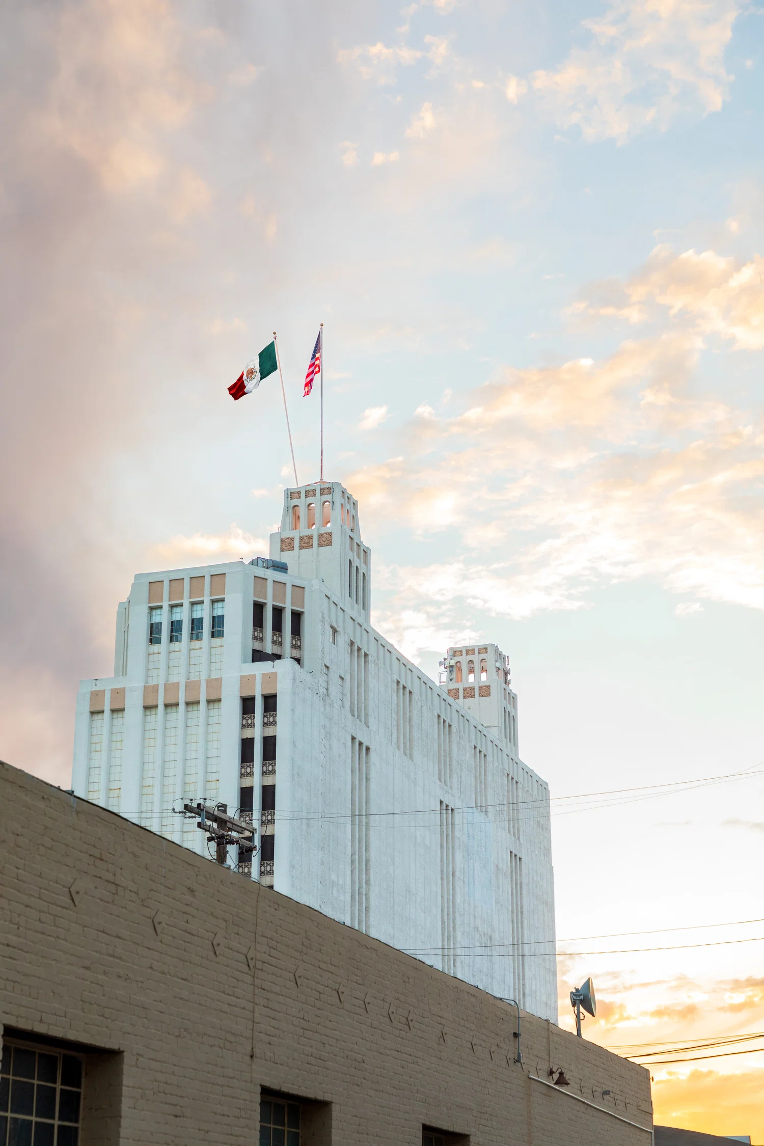 This image includes a photo of a building during sunset with an American flag on top with a photoshopped Mexican flag next to it.