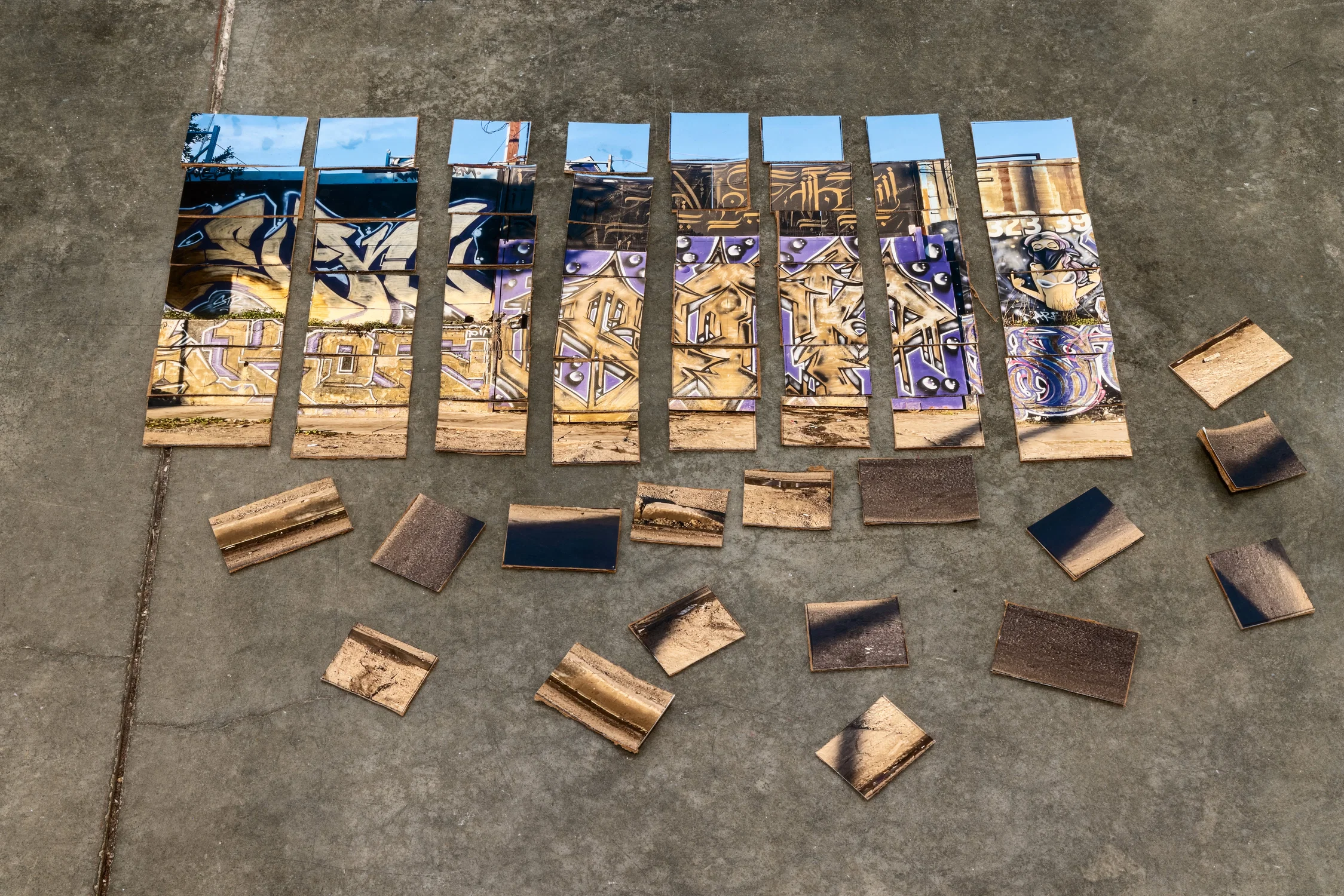 This image includes photo of a business with graffiti that has been cut up and adhered in 2x2 squares onto cardboard and placed on the floor.