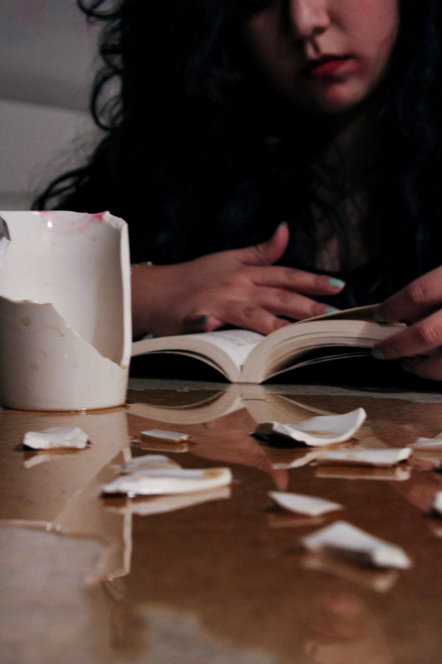 A photograph of a woman casually reading a book while there is a shattered coffee mug with spilled coffee.