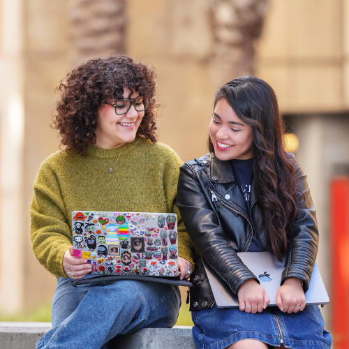 Two students looking at laptop together outside