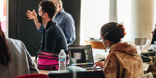 A student at a computer while others discuss her 3d digital modeling project