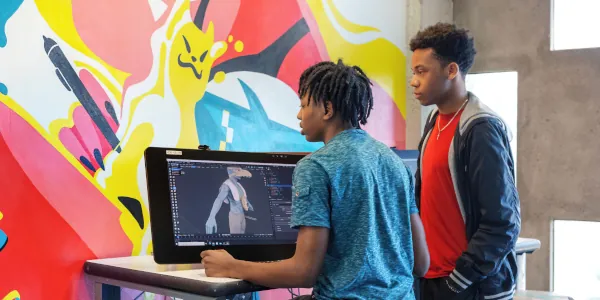 Two students at at computer working on a character for a game