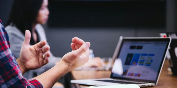 Man (mostly his hands) in foreground and out of focus woman in background at a buisiness meeting