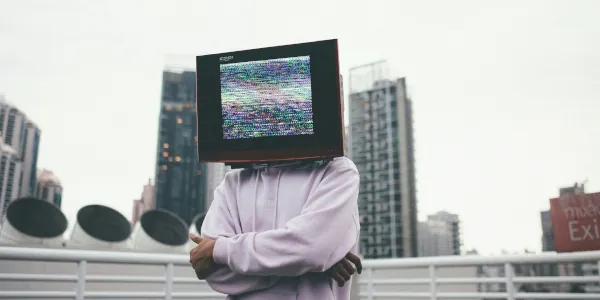 Man standing on a rooftop with folded arms an his head replaced by a computer monitor.