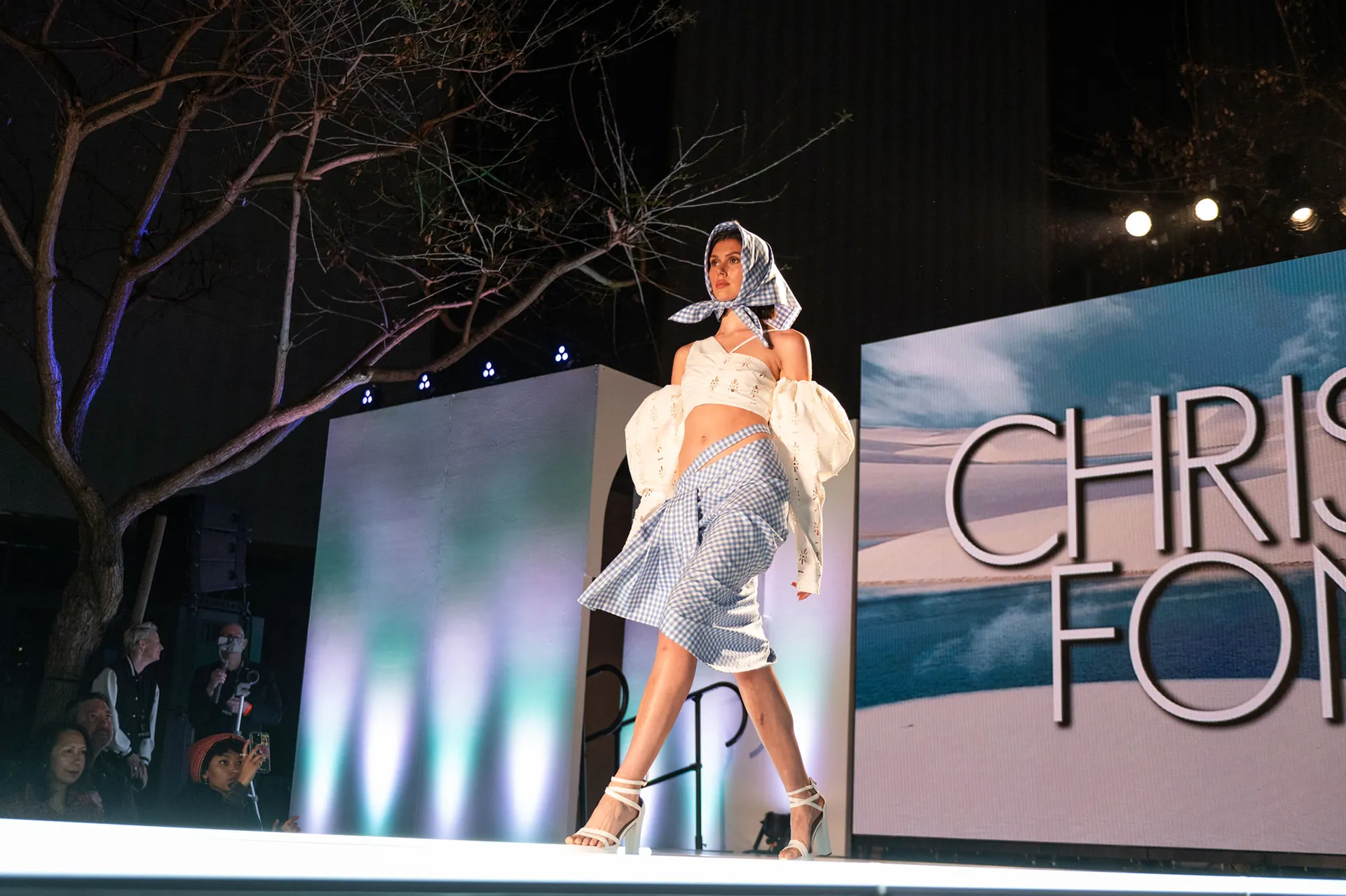 Model at fashion show wearing light blue checkered pattern and white halter