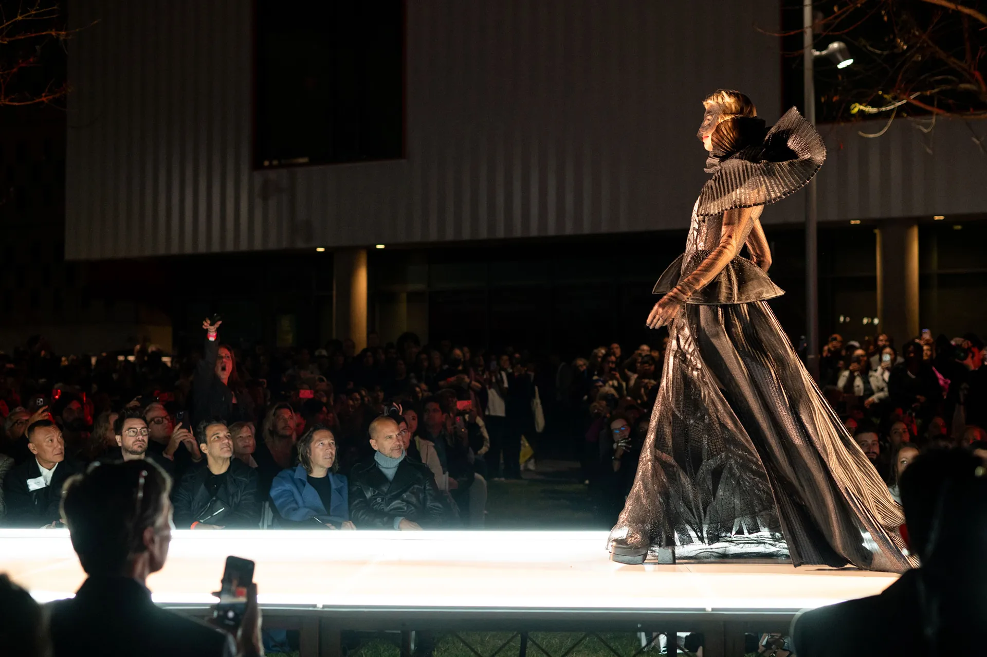 Model on a runway wearing a costume-style outfit with a black mask