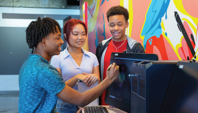 Three students working on digital artwork together at computer station