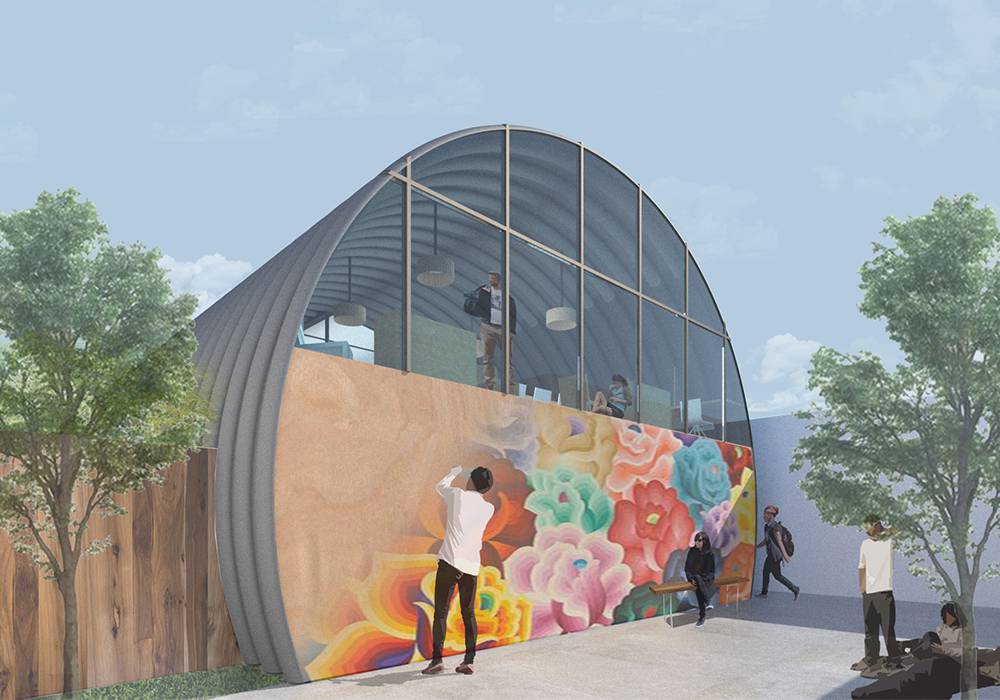 This image depicts the exterior of the homeless youth shelter where people are hanging out outside as a man paints a mural on the end wall of the quonset hut. 