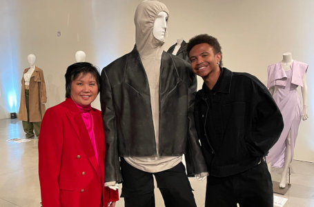 A man and woman posing with a male fashion mannequin wearing
    black jeans and a black leather-like jacket over a light tan hooded garment