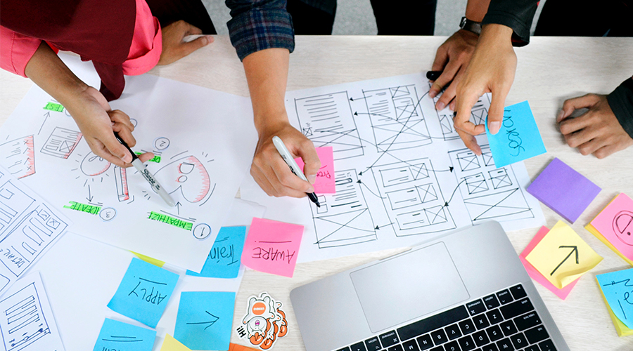 A team of designers work on UX/UI projects on a desk with drawings and post-it notes.